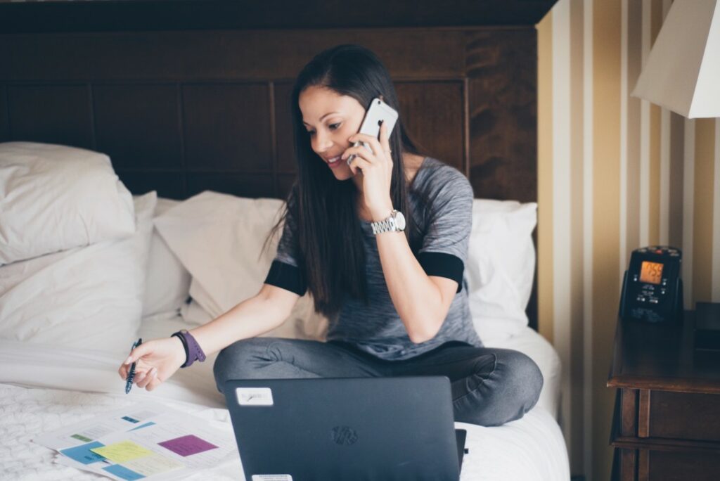 woman talking on the phone with computer on the bed