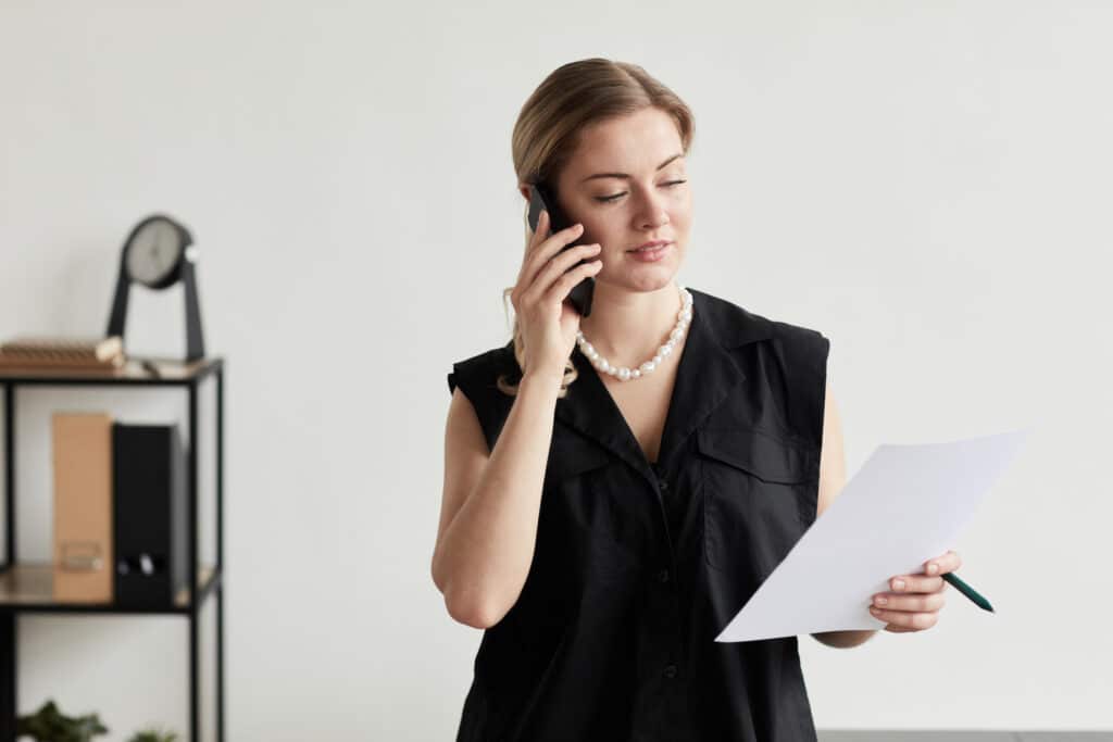 Waist up portrait of blonde successful businesswoman speaking by smartphone in graphic black and white interior, copy space