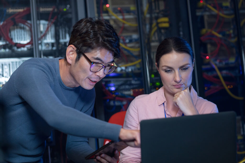 male and female engineers discussing over a laptop in a computer server room