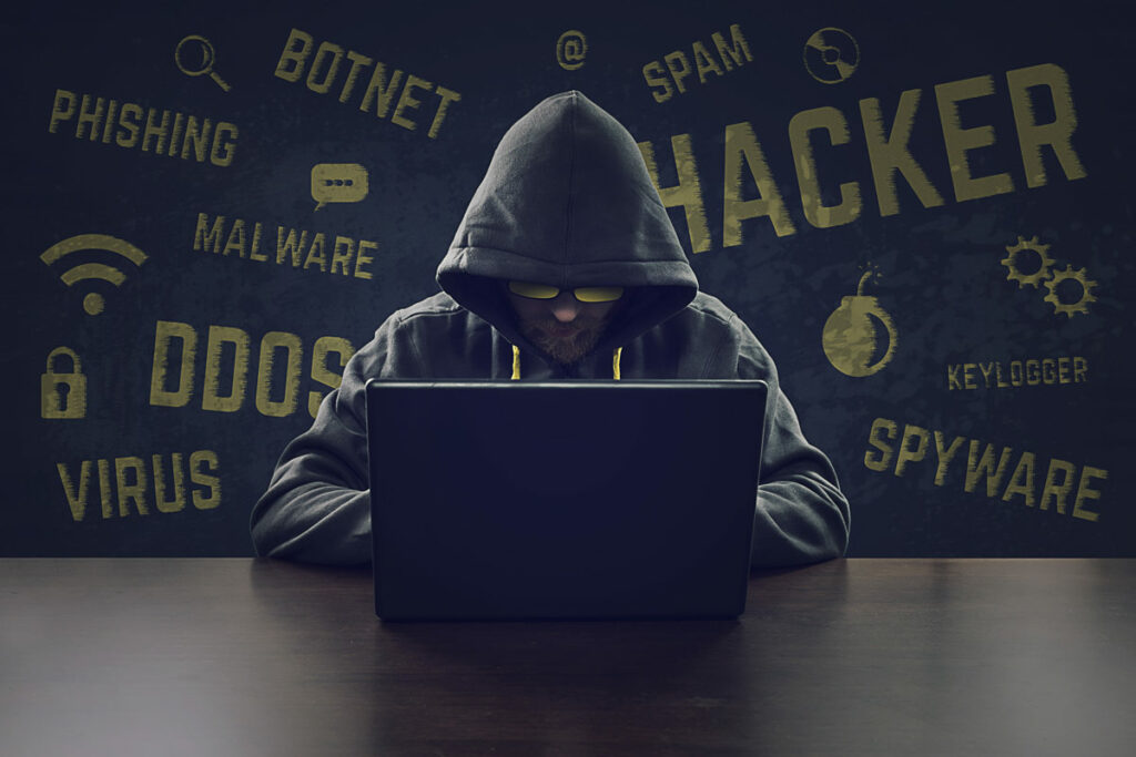 Computer hacker with a hoodie on sitting at a desk with sunglasses