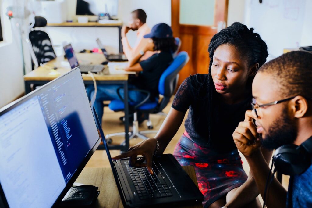 Two people sit together at a desk and look at a computer