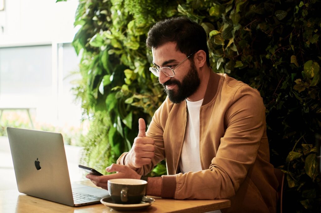 A man in a brown jacket gives a thumbs up to someone on his computer screen