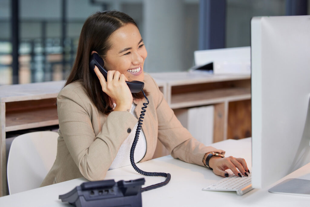 Young woman at work using a telephone business system while she works on a computer